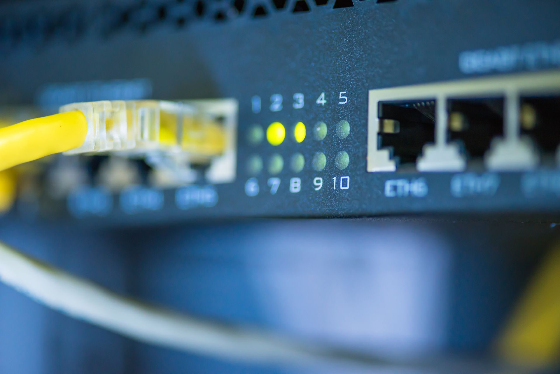 Close-up of a network switch with a yellow Ethernet cable plugged in, lights illuminated, indicating active connections.