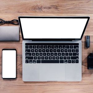 Laptop, phone, external hard drive, and other tech devices on a wooden table.