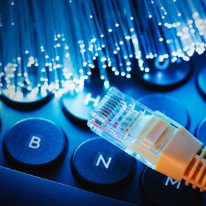 Close-up of an Ethernet cable over a keyboard, with optical fibers in the background, all bathed in blue light.
