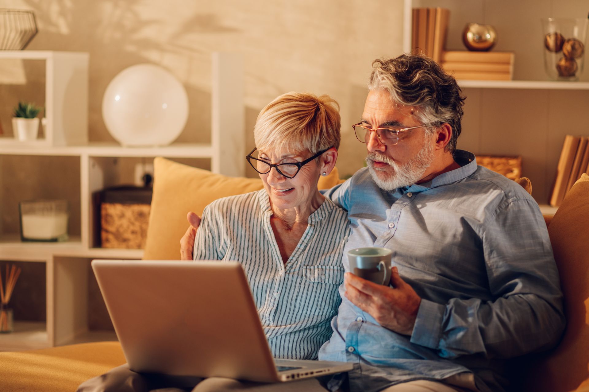 Couple on a couch looking at a laptop together, lit by warm light.