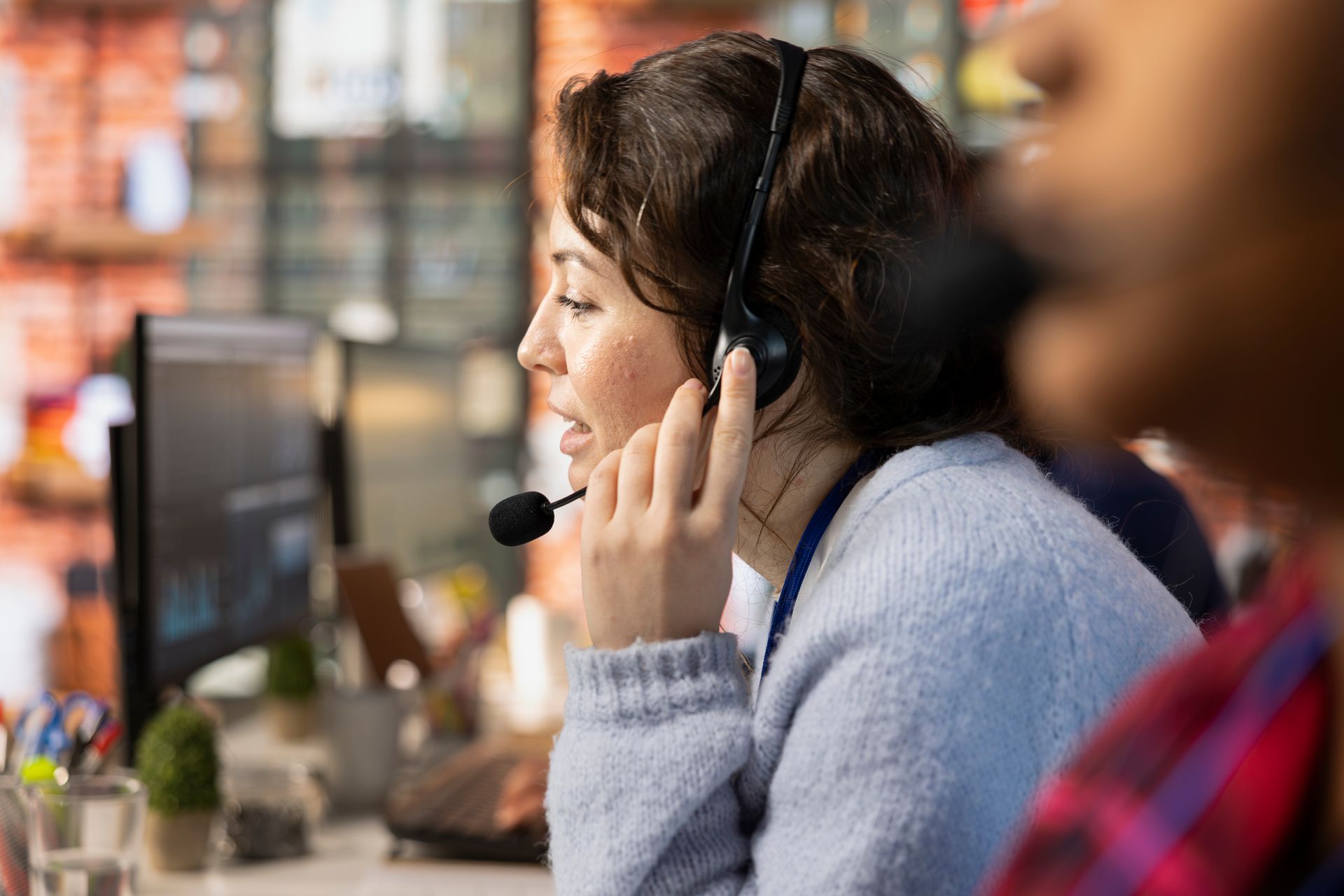 Woman wearing a headset, speaking, at a desk with a computer, indoors.