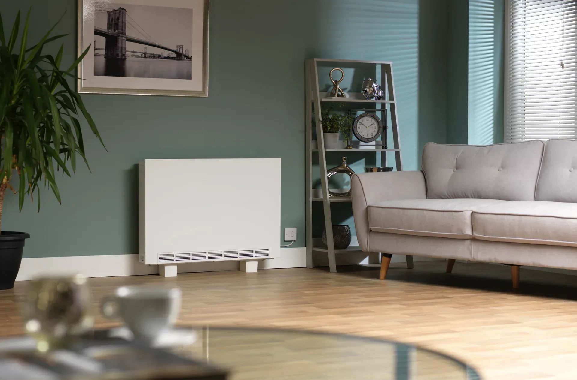 White storage heater in a living room; green wall, grey sofa, wooden floor.