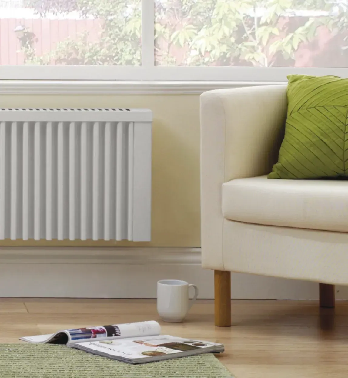 White radiator on a wall, next to a cream armchair and window. Magazine and mug on the floor.