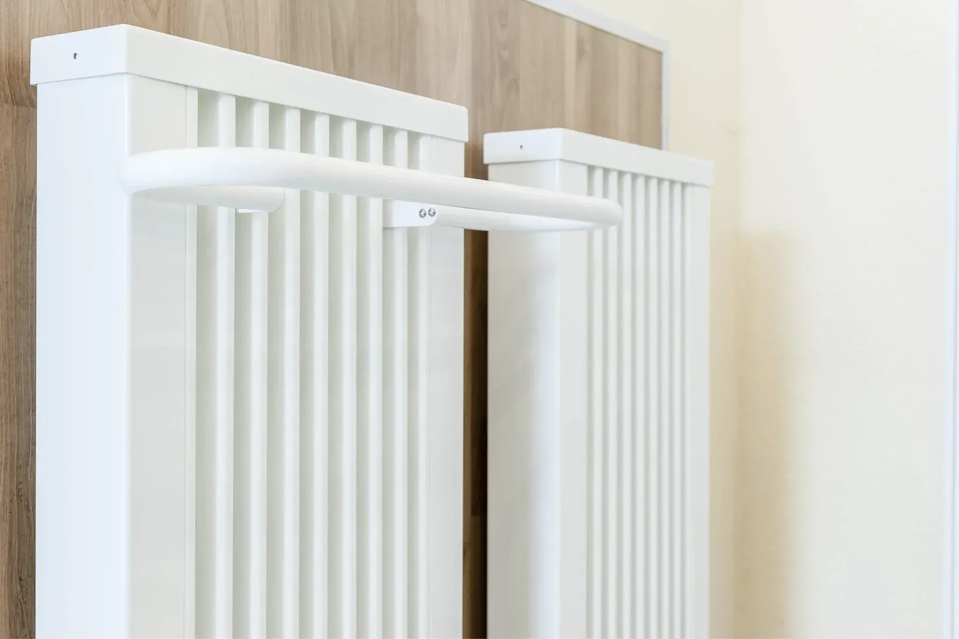 Two white vertical panel radiators with a towel bar, mounted on light wood paneling.
