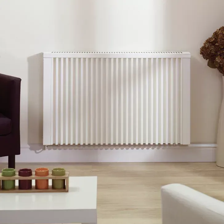 White wall-mounted radiator in a living room, with a sofa, coffee table, and vase.