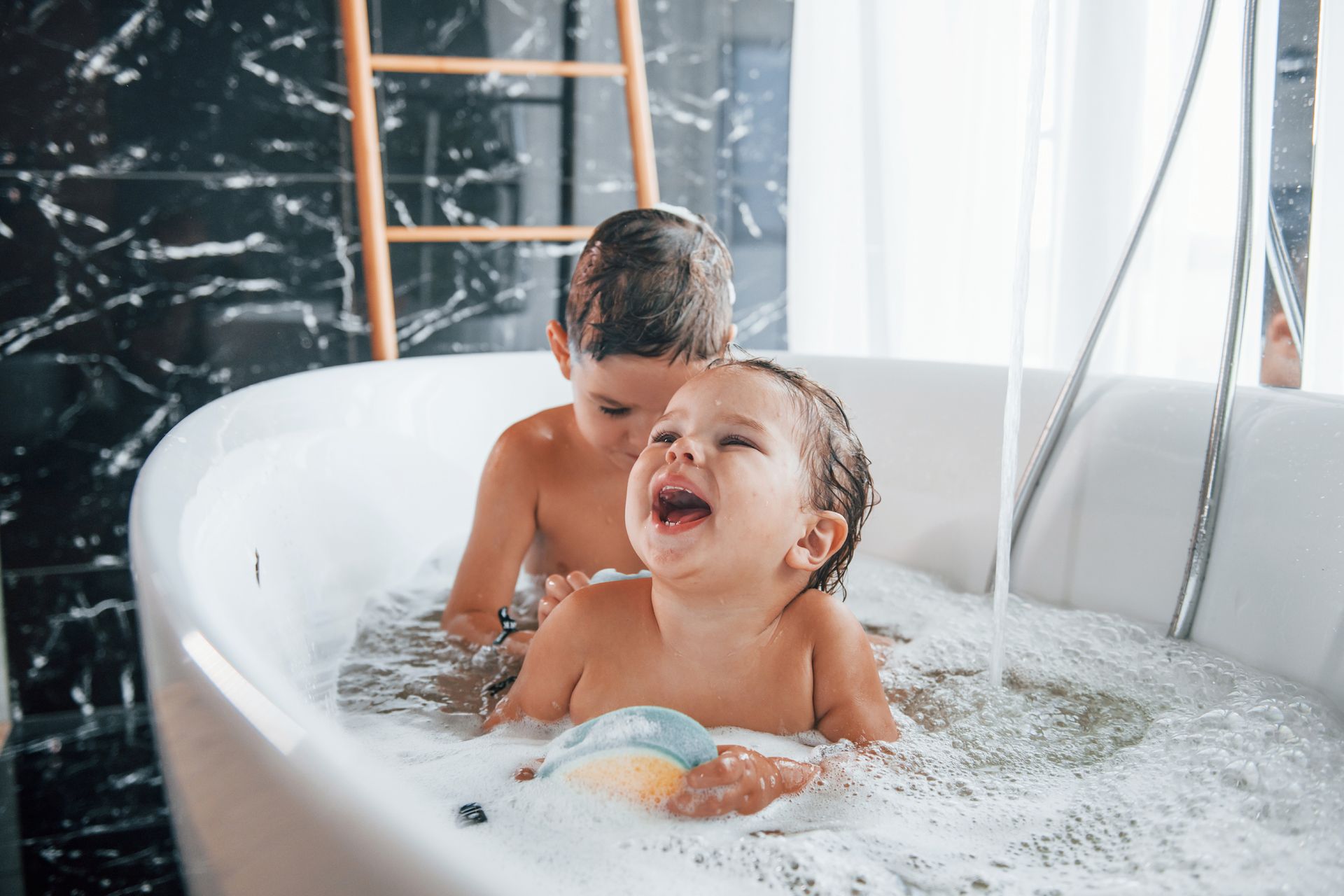 Two children are taking a bath together in a bathtub.