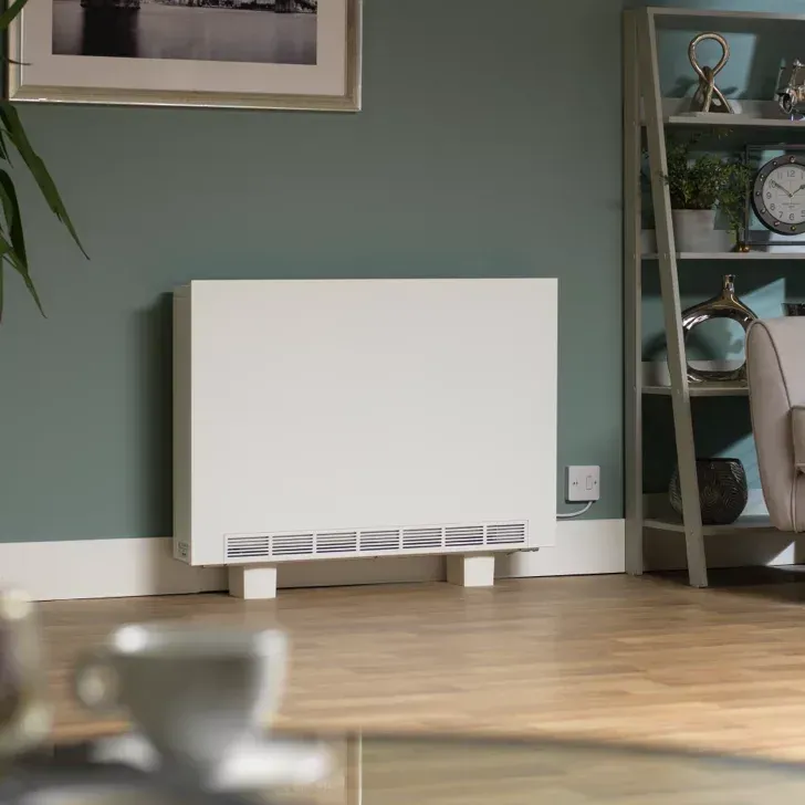 White storage heater against a teal wall in a living room with wooden floor, shelves, and framed art.