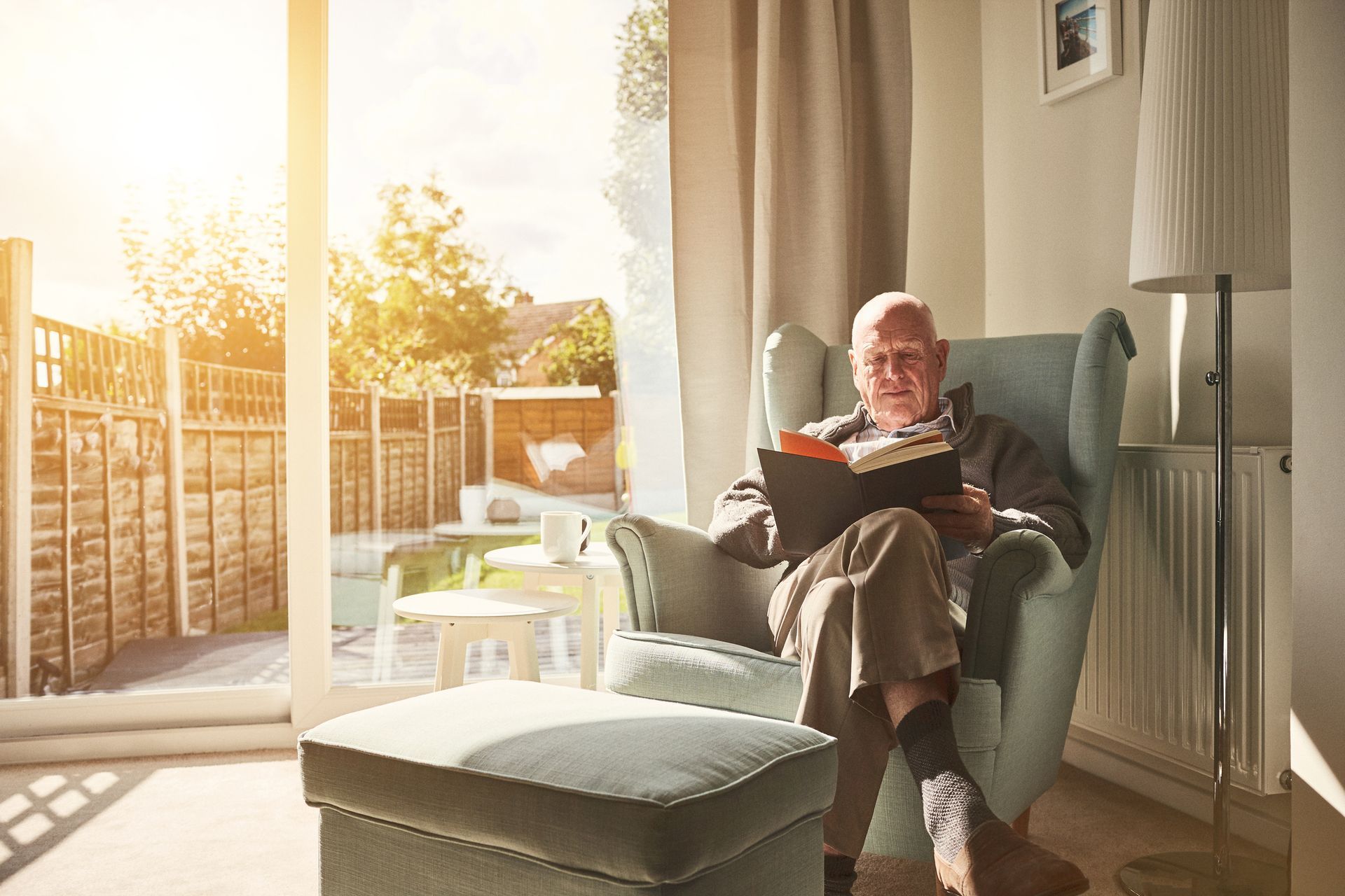 An elderly man is sitting in a chair reading a book.