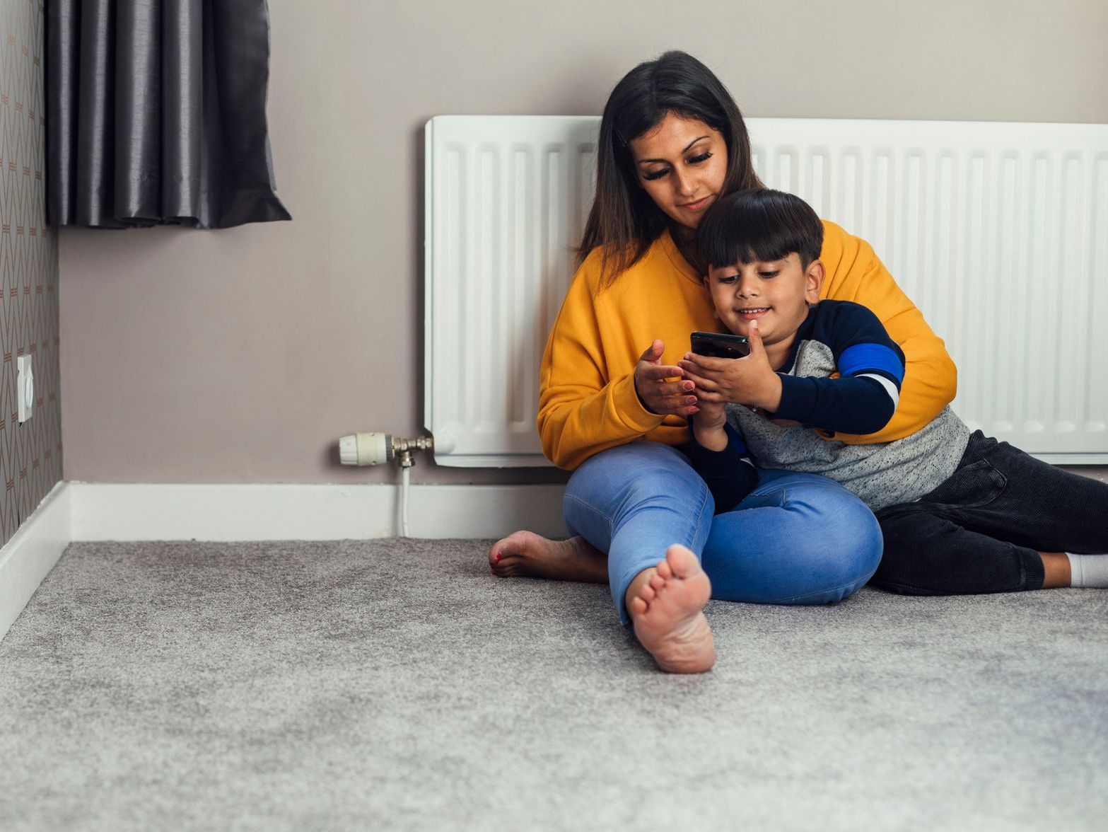 A woman and a child are sitting on the floor looking at a cell phone.