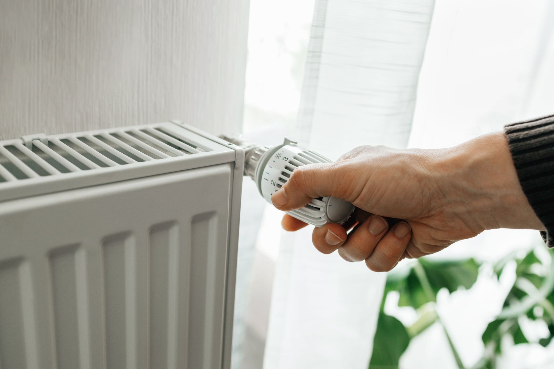 A person is adjusting a thermostat on a radiator.