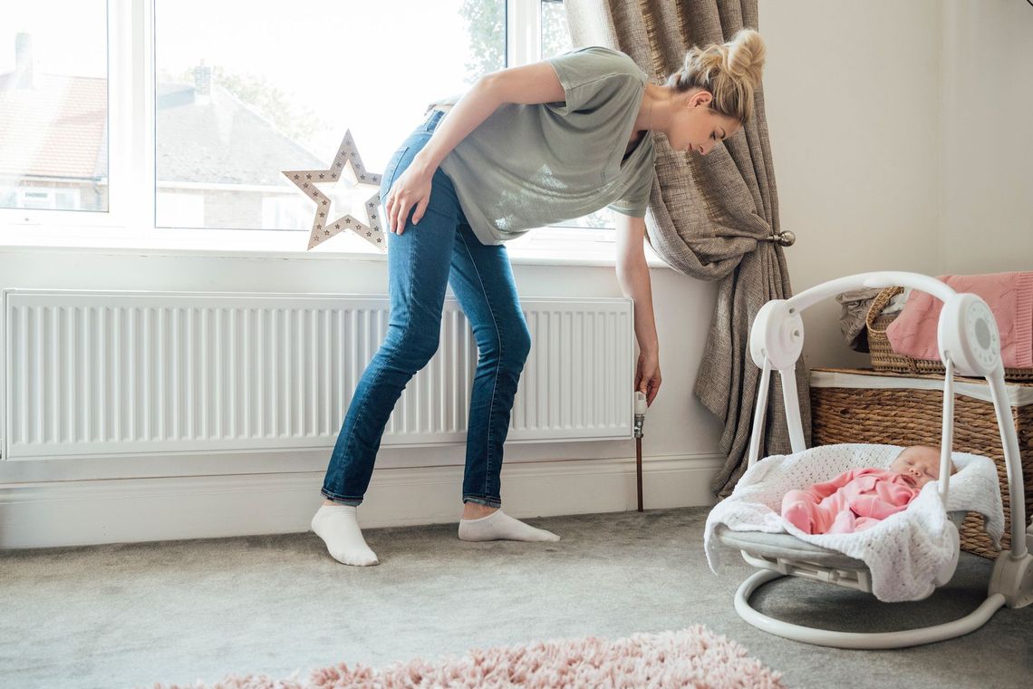 A woman is standing next to a baby in a swing in a room.