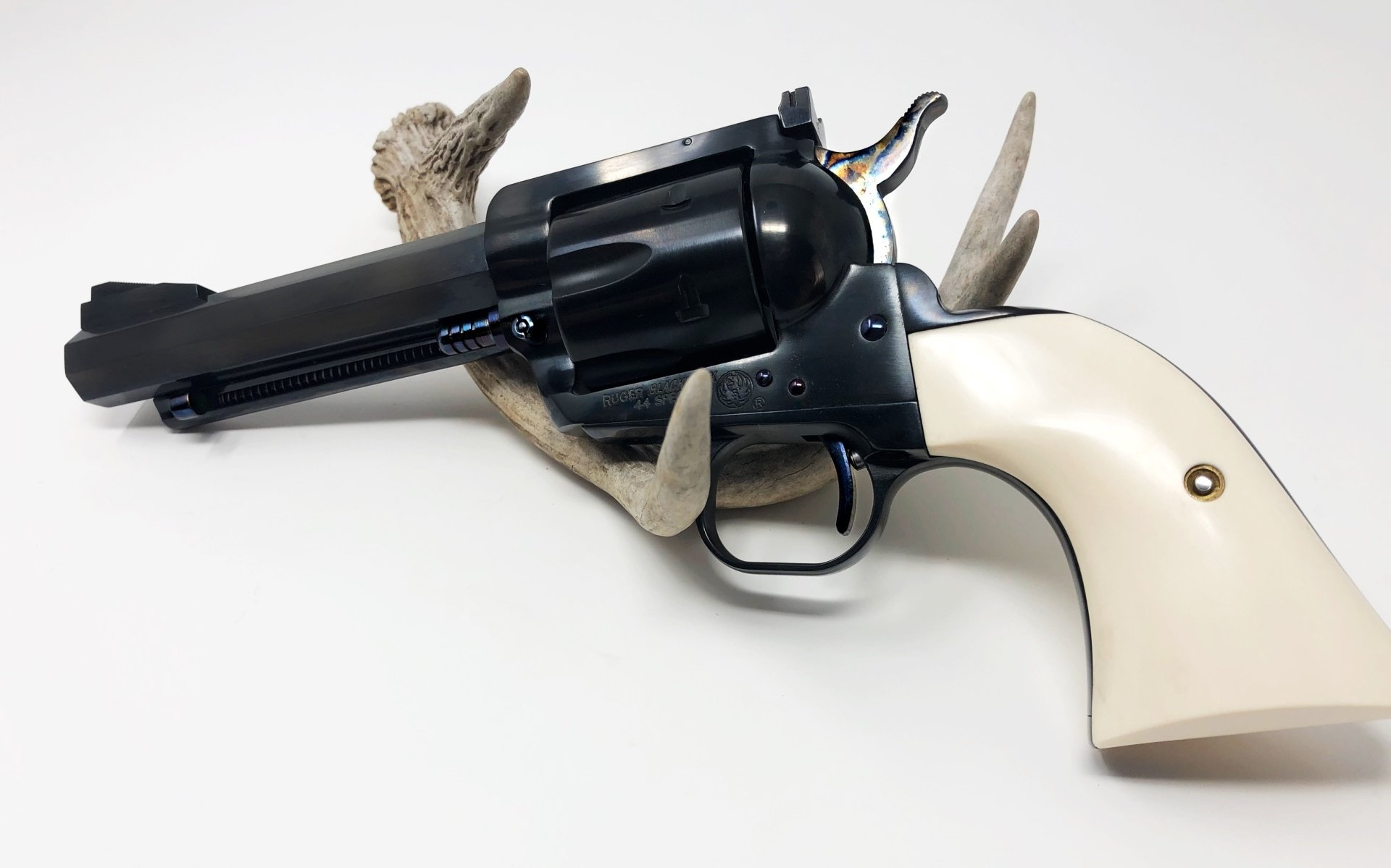 Black and white revolver pistol with ivory grip resting on a piece of wood against a white background.