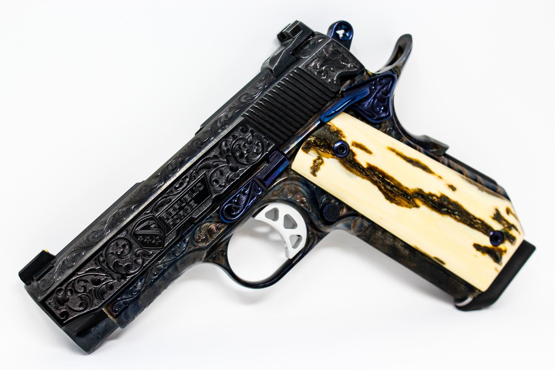 Elaborately engraved dark pistol with cream and brown grip, against a white background.