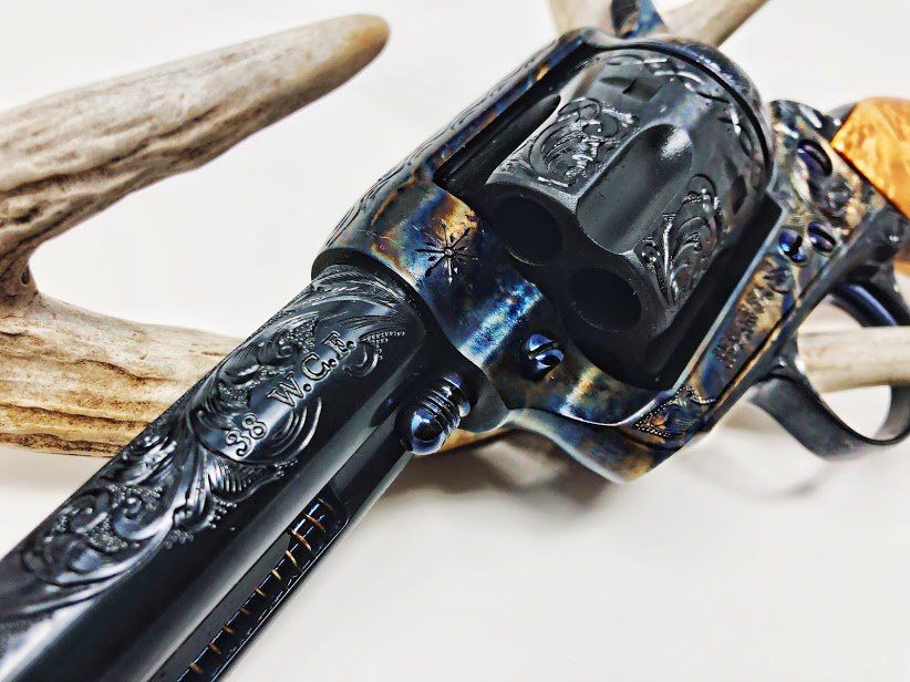 Close-up of a blued, engraved revolver with gold accents, resting on a white surface with antlers.
