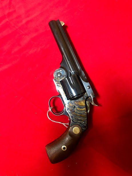 Antique revolver with wood grip and ornate metalwork, set against a red background.
