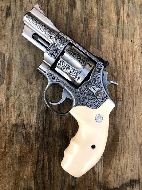 Engraved stainless steel handgun with ivory-colored grips on a wooden surface.