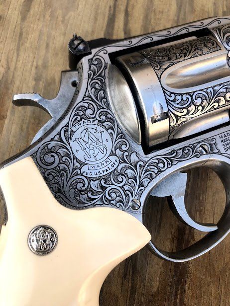 Engraved Smith & Wesson revolver with ivory-colored grips and floral scrollwork, close-up on wood.