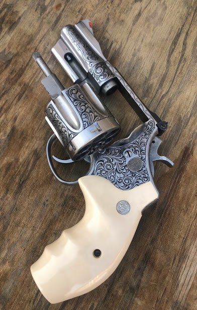 Engraved silver revolver with white grip, on a wooden surface.