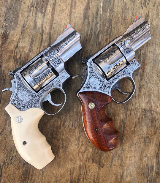 Two engraved silver revolvers with different grips on a wooden surface.