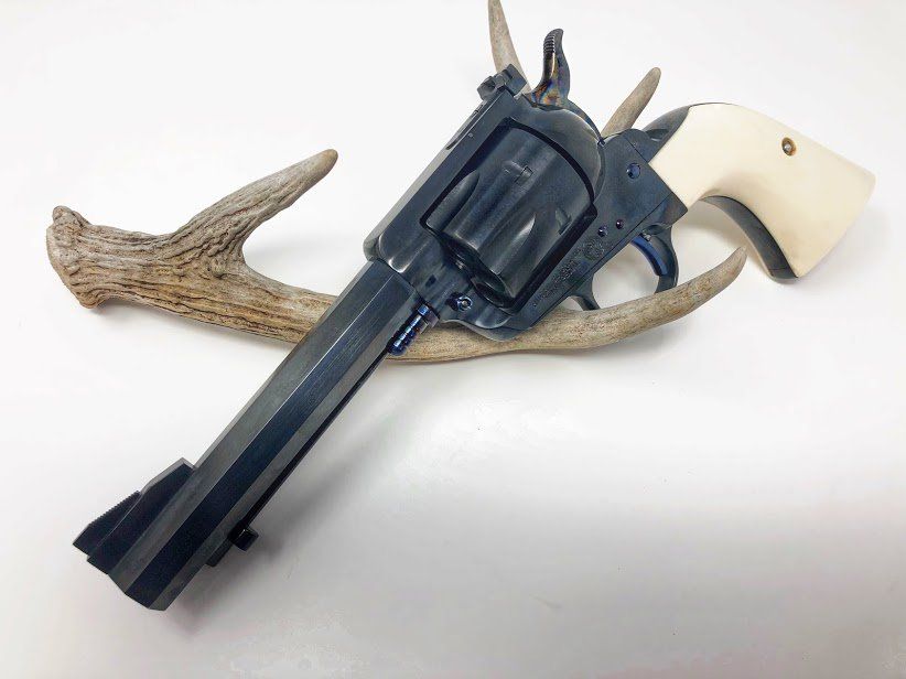 Black revolver with ivory grip resting on a dried antler against a white background.
