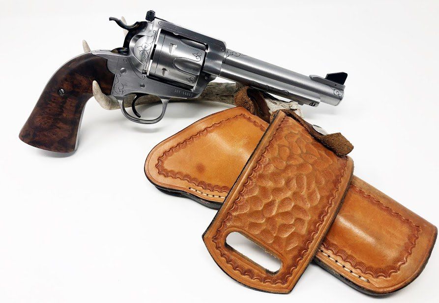 Revolver pistol and two brown leather holsters on a white surface.