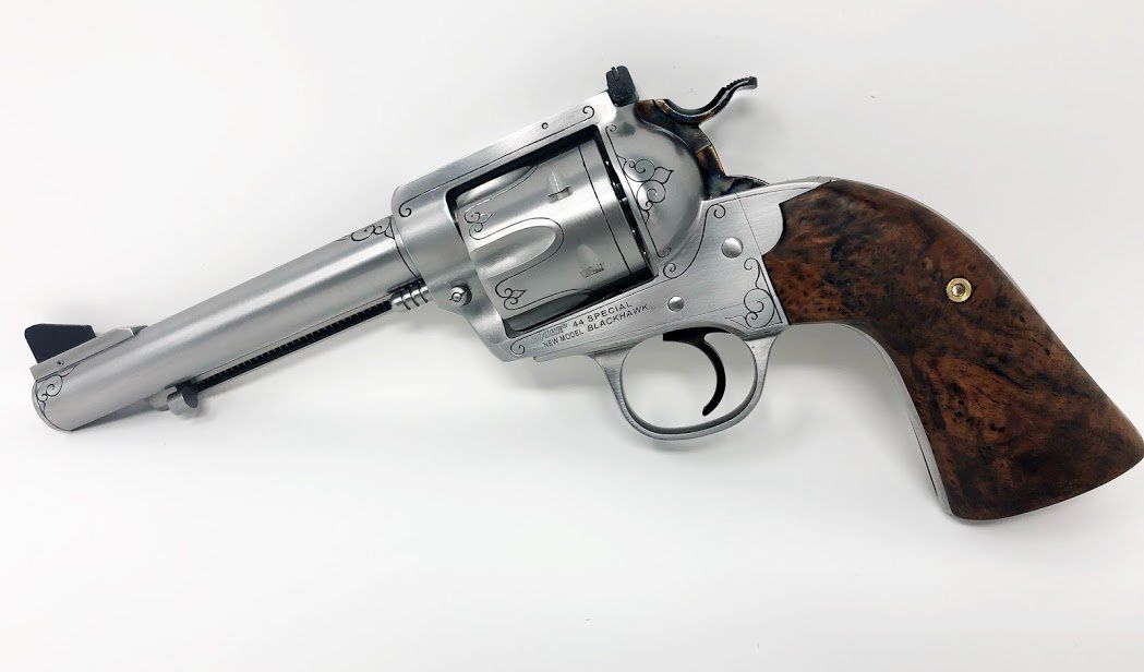 Silver and wood-handled revolver on white background with decorative engravings.