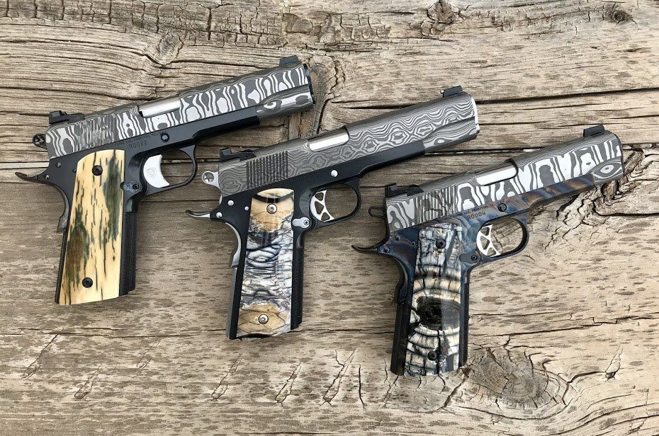 Three customized pistols with patterned slides and colorful grips resting on a wooden surface.