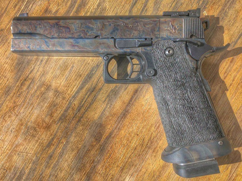 Pistol with a patterned, blue-brown finish and black textured grip on a wooden surface.