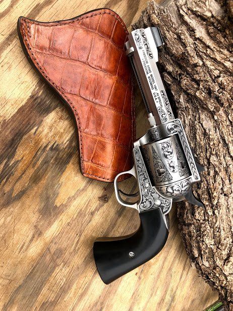 Engraved revolver with a black handle and a brown alligator-skin holster on a wood surface.
