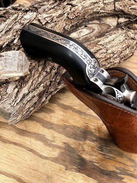 Black antique pistol with silver detailing, in a brown leather holster on wood.