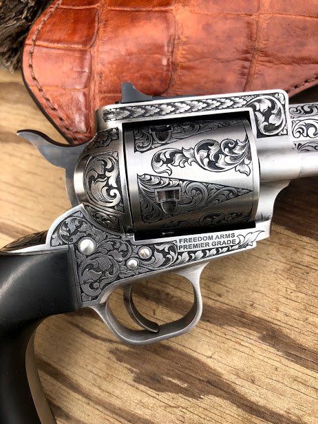 Engraved silver revolver with wooden handle, set against a textured brown leather holster and wood grain background.