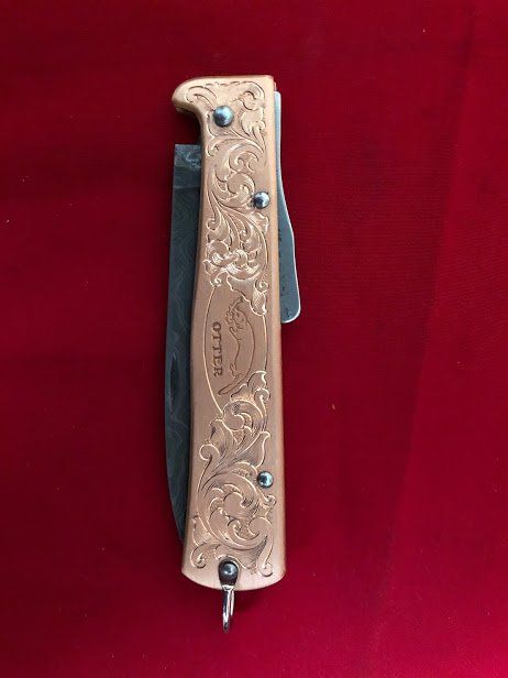 Ornate gold-toned folding knife with floral engravings, corkscrew, and bottle opener on a red background.