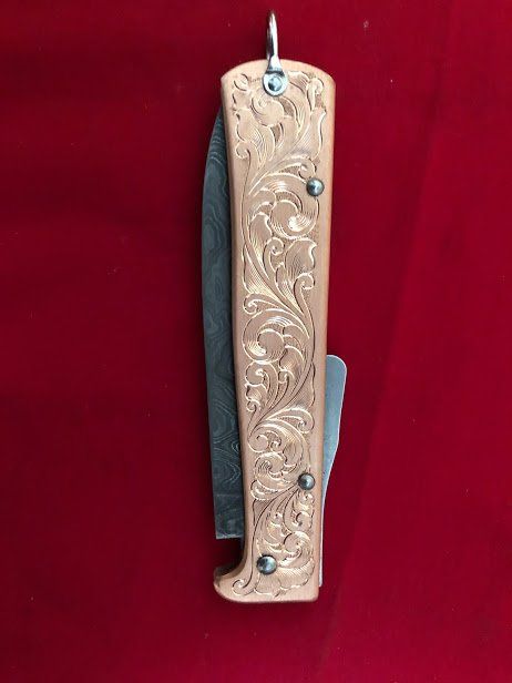 Engraved folding knife with a floral design on a red background.