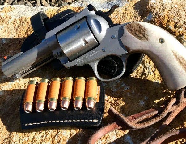 Silver revolver with brown handle, resting next to a leather ammo holder with bullets.