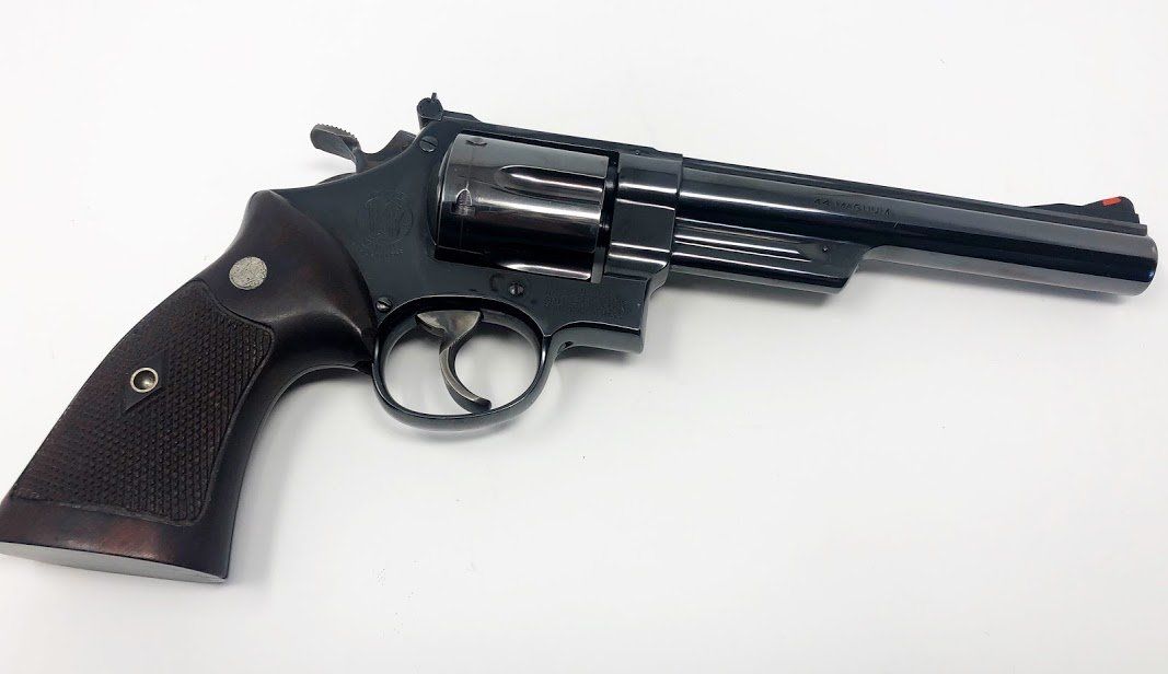 Black revolver handgun with a dark wooden grip on a white surface.