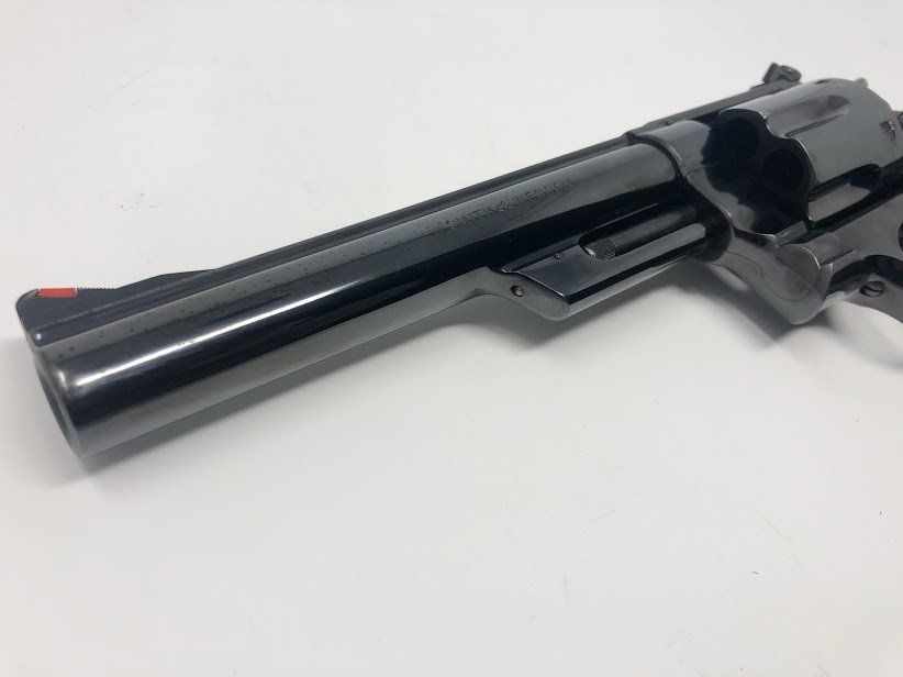 Black revolver pistol with red front sight, on a white surface.