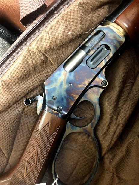 Lever-action rifle with ornate bluing and a brown wood stock, resting on textured fabric.