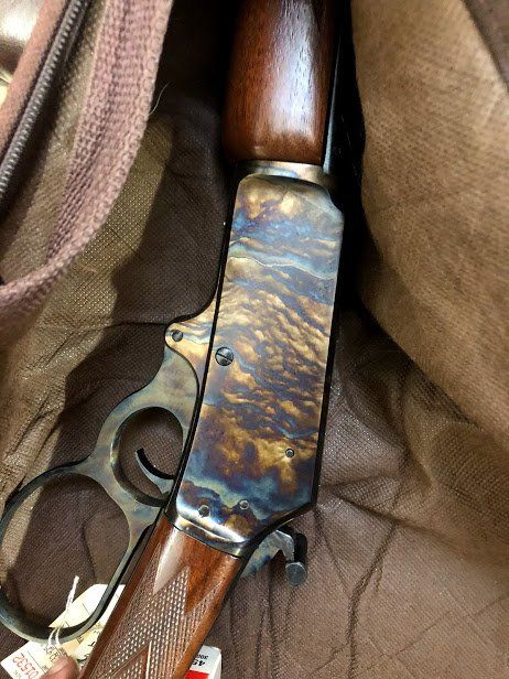Lever-action rifle with blued receiver, wood stock, in a brown carrying case.