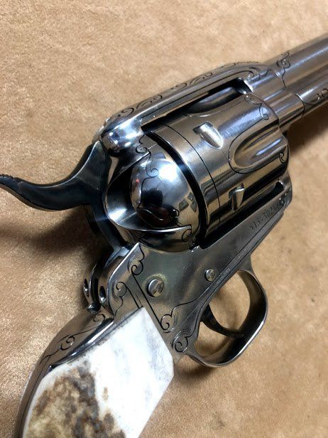 Close-up of a polished silver revolver with etched details and an antler handle, resting on a brown surface.