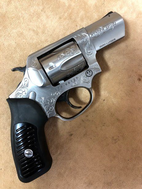 Stainless steel revolver with floral engraving on a brown surface.