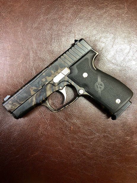 Black handgun with camo pattern on brown leather surface.
