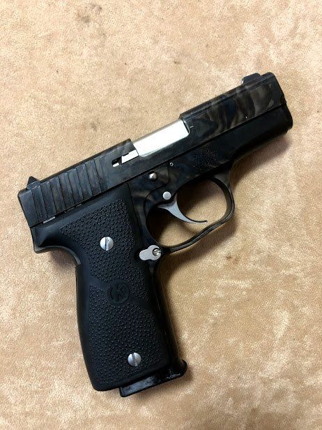 Black and gray handgun, resting on a light brown, textured surface.