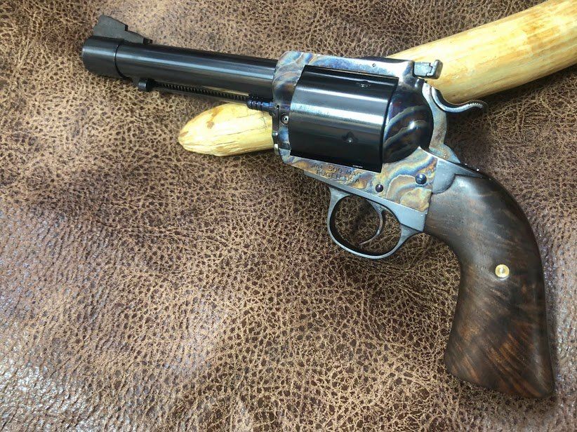 A custom revolver with dark blue barrel, dark wood grip, and decorative metalwork, resting on a leather surface.