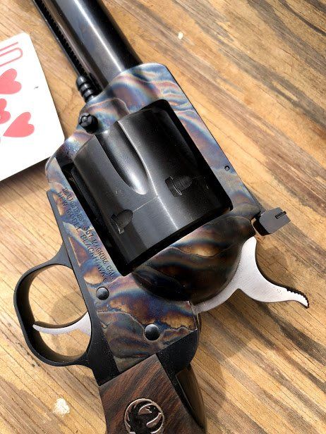 Close-up of a Ruger revolver with a blued frame and wood grips, next to a playing card.