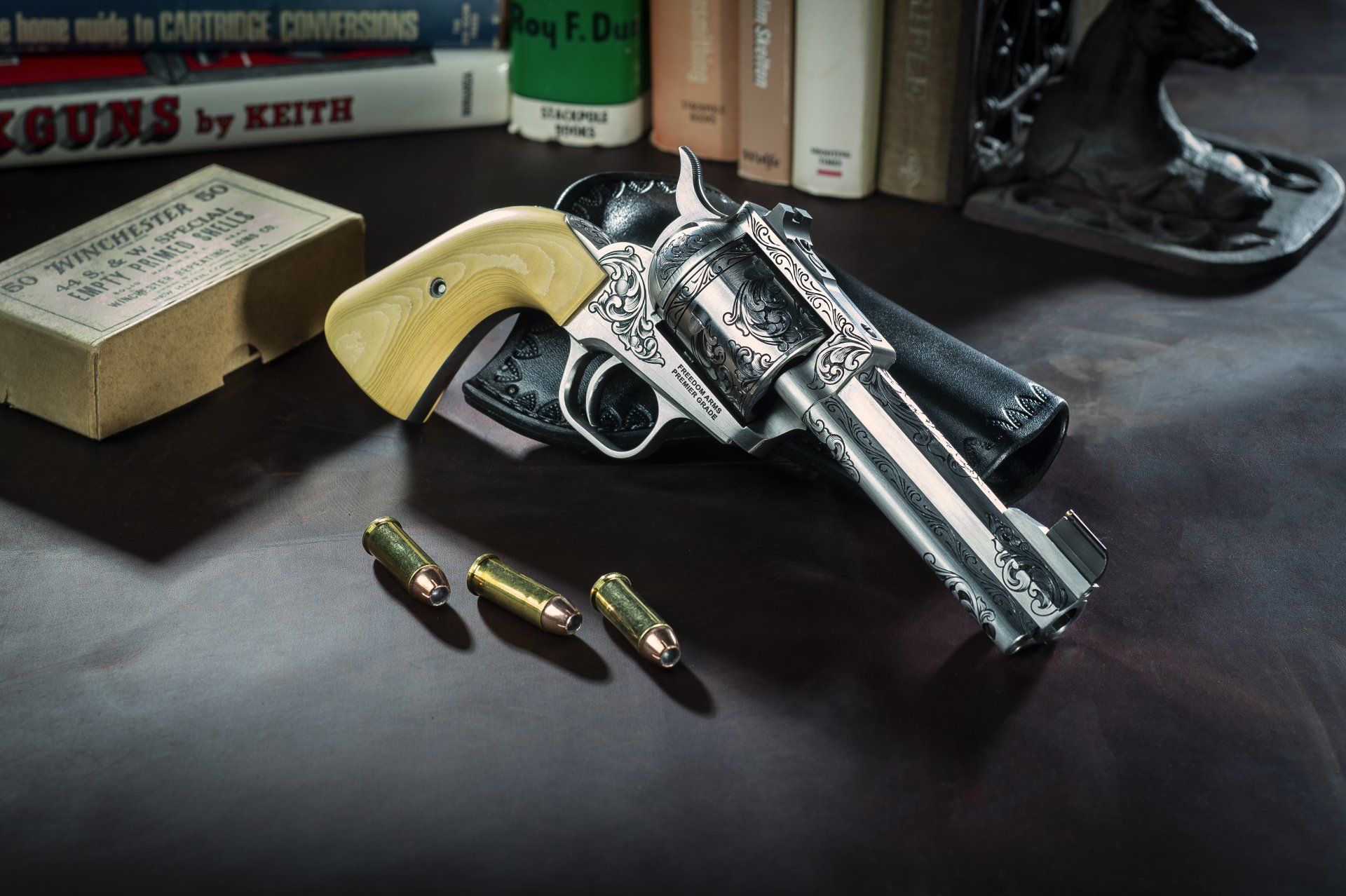 Engraved revolver with ivory grip on a dark surface, next to bullets and a box of ammunition.