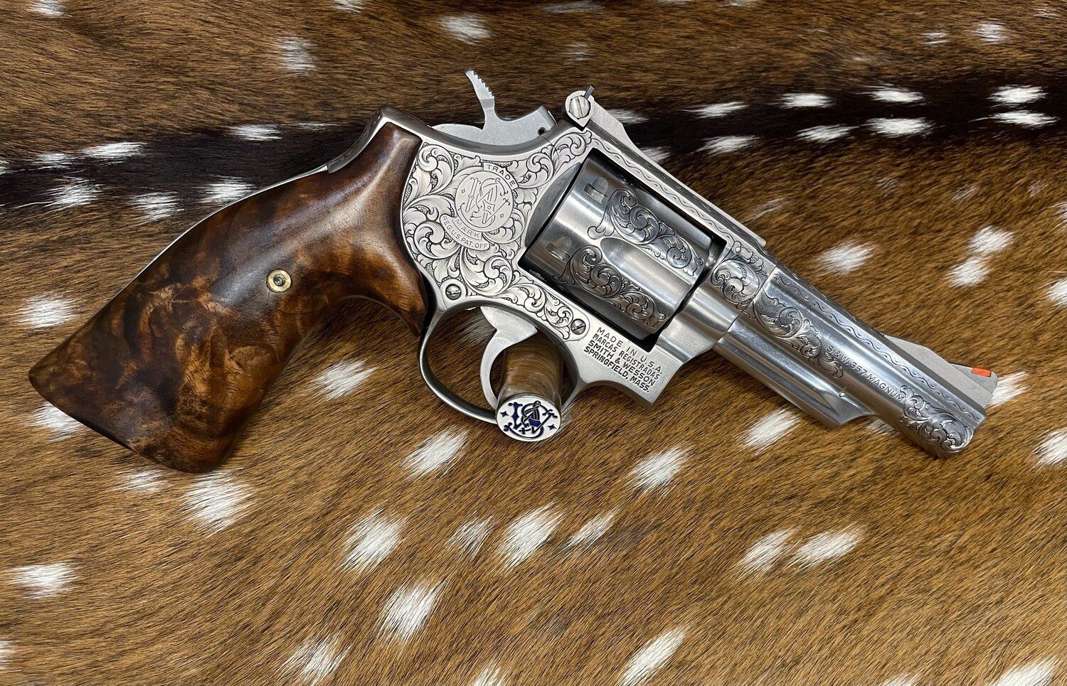 Engraved silver revolver with wooden grip, resting on a spotted animal hide.