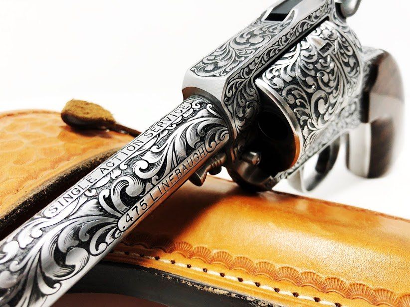 Engraved silver revolver with detailed floral patterns, resting on a tan leather holster.