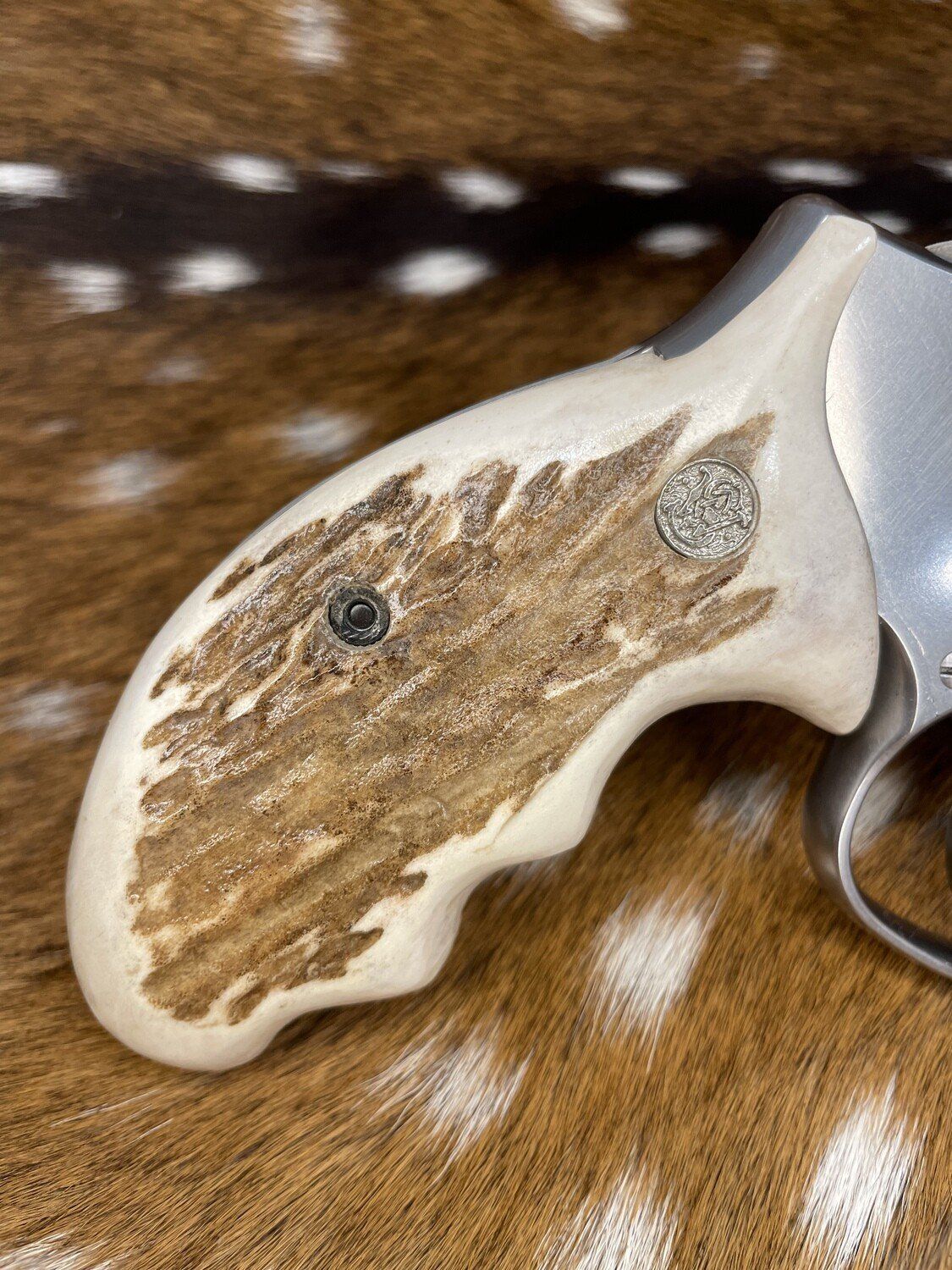 Ivory-colored revolver grip with a light brown antler inlay.  Silver gun metal is visible.