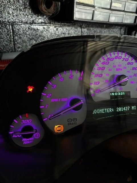 Car dashboard with purple backlighting; speedometer, tachometer, and other gauges illuminated.