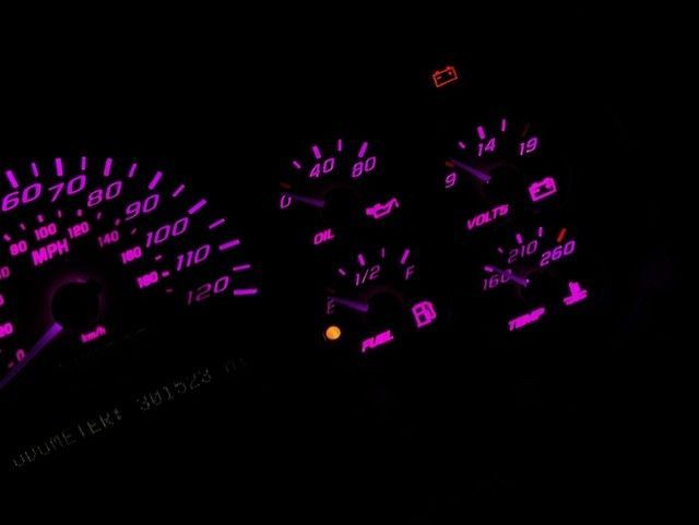 Glow-in-the-dark car dashboard with illuminated purple gauges showing speed, oil, fuel, and voltage.